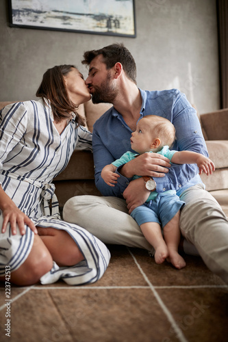 Happy couple holding their baby boy and kissing at home.