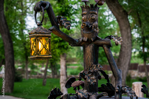 Modest, metal, rustic and fabulous lantern with warm orange and yellow light. On the background of a fabulous green forest, outdoors.