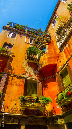Fototapeta Naklejka Na Ścianę i Meble -  Balconies with beautiful plants and bright colors: old residential orange house of the historic district of Venice – summer photo with clear blue sky