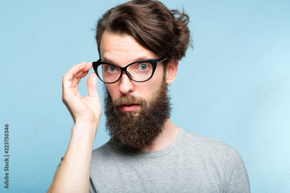 eccentric teacher or quirky it guy. bearded hipster dude wearing cat eye  glasses. stylish modern fashionist. portrait of a geeky foppish man on blue  background. Stock Photo