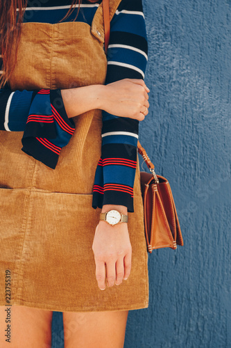 close up, young fashion blogger wearing a corduroy dress and a white and golden analog wrist watch. checking the time, holding a beautiful  leather purse. street style fashion details. 