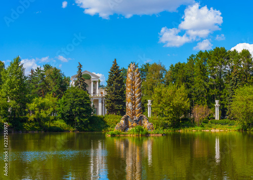 Kolos fountain (Spike) in a large pond on the background of beautiful trees with an old building of Soviet architecture at the park in VDNKH (Moscow, Russia)