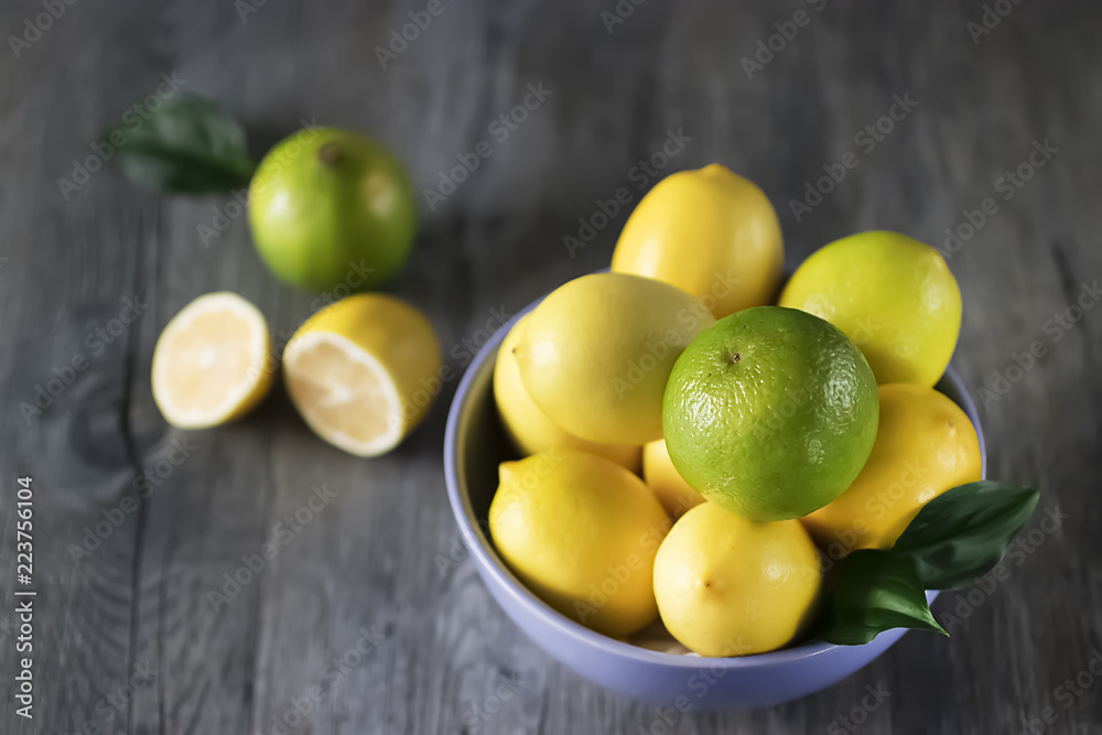Fresh ripe lemons and limes in blue bowl on gray wooden table.