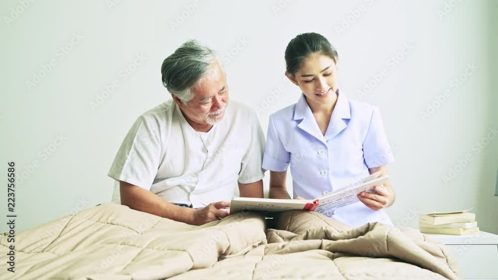 Young beautiful female nurse reading book to senior man. Asian woman reading book to old asian man with white beard in bed. Senior home service, care taker concept. Young beautiful female nurse reading book to senior man. Asian woman reading book to old asian man with white beard in bed. Senior home service, care taker concept.