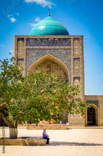 A woman sits under a tree in front of the Kalon Mosque in Bukhara, Uzbekistan