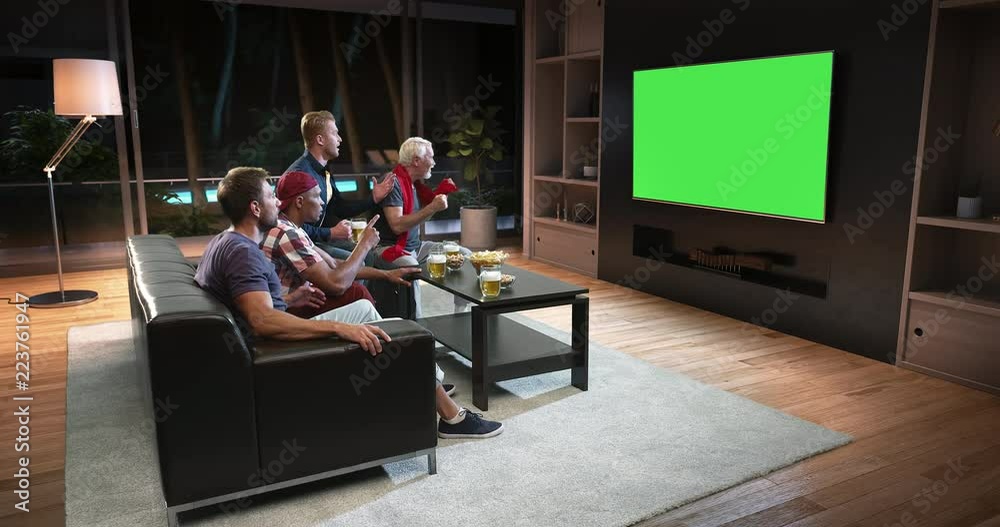 A group of fans is watching a TV and celebrating some joyful sports moment, sitting on the couch in the living room. The living room is made in 3D. TV is in green for further editing. A group of fans is watching a TV and celebrating some joyful sports moment, sitting on the couch in the living room. The living room is made in 3D. TV is in green for further editing.