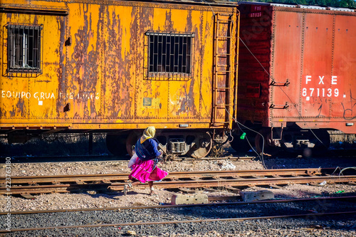 CREEL, MEXICO-Jan 2016: A native Raramuri woman in bright clothing runs across railway tracks while waiting for the El Chepe Copper Canyon train at Creel railway station in Chihuahua, northern Mexico photo