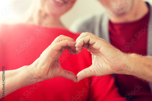 relationships, love and old people concept - close up of senior couple showing hand heart gesture