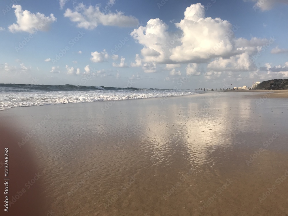 Seascape, blue waves with white foam on the beach with golden sand under a blue sky