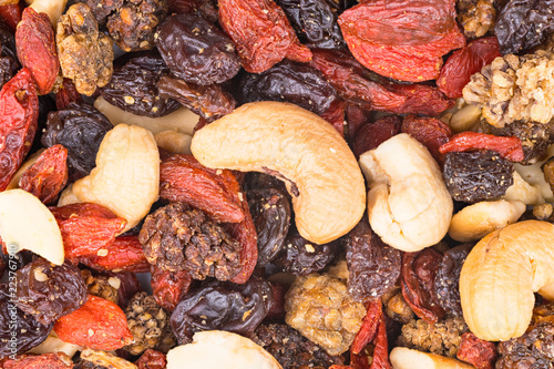 Mixture of cashew seeds and sweet dried berries close-up. Pile of roasted nuts, dry mulberries, raisins and goji fruits. Culinary background. Yummy vegetarian snack. Decorative brown-reddish texture.