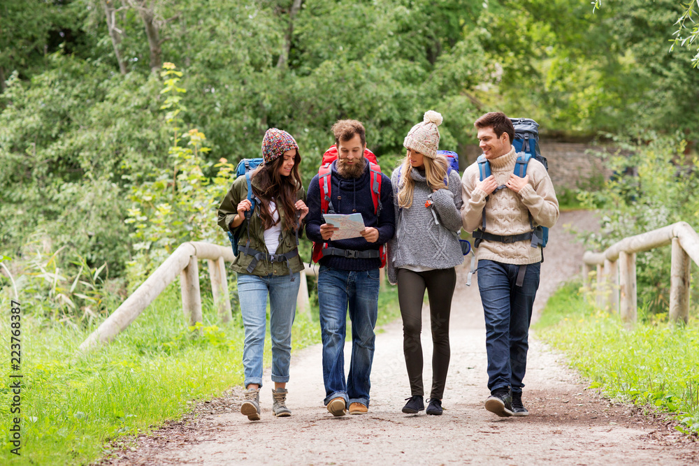travel, tourism, hiking and people concept - group of happy friends or travelers with backpacks and map walking along road