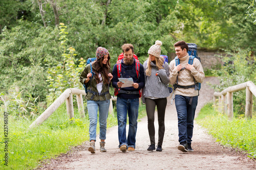 travel, tourism, hiking and people concept - group of happy friends or travelers with backpacks and map walking along road