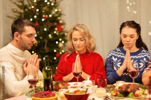 holidays and celebration concept - friends holding hands and praying before christmas dinner at home