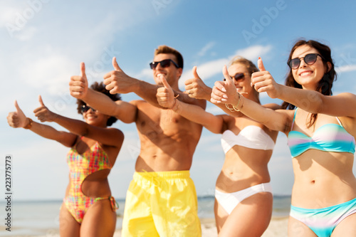 friendship, summer holidays and gesture concept - happy friends on beach showing thumbs up