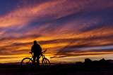 Silhouette of a cyclist on the background of a magnificent sunset. The guy is standing with the bike and watching the sunset