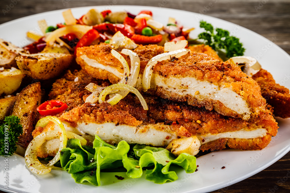 Fried pork chop with potatoes and vegetable salad on wooden background