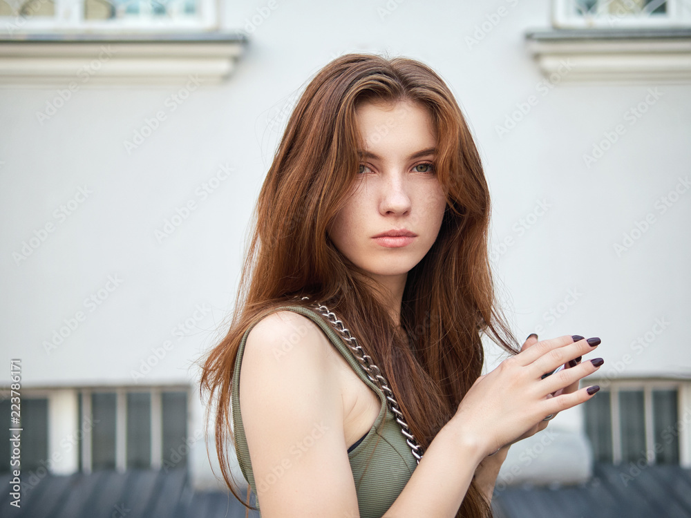 Art portrait of a young pretty redhead woman posing outdoors in green dress against city building background Art portrait of a young pretty redhead woman posing outdoors in green dress against city building background