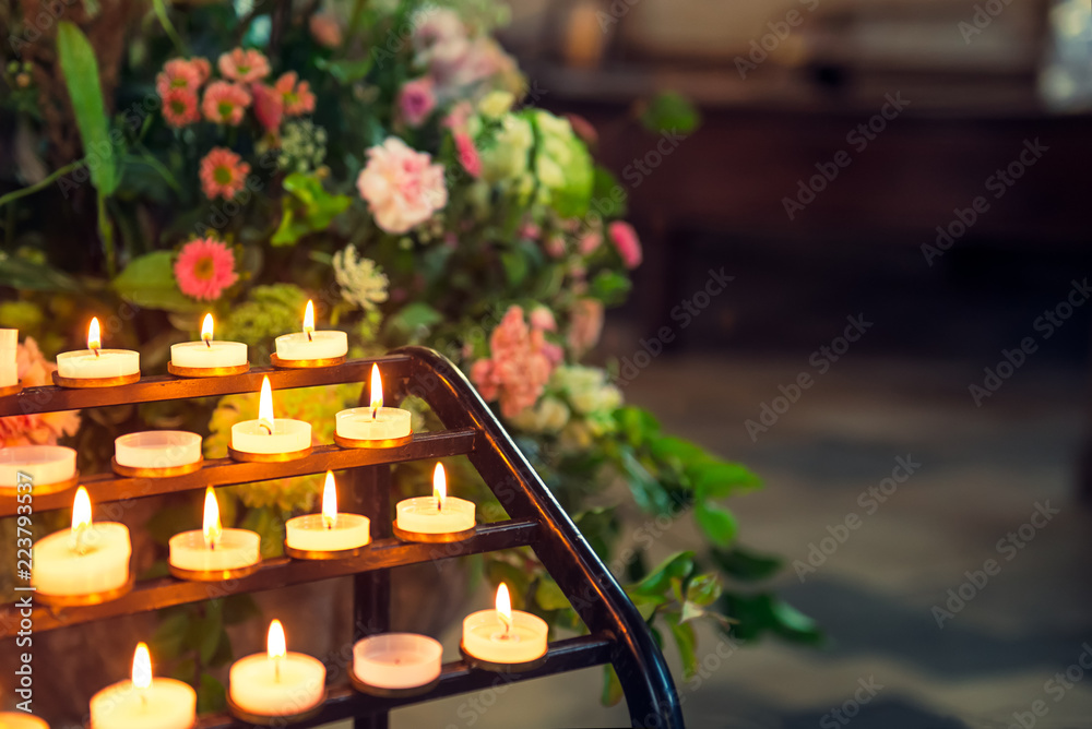 Close up burning candles in sconces on background of flowers and catholic cathedral interior. Selective focus, copy space. Close up burning candles in sconces on background of flowers and catholic cathedral interior. Selective focus, copy space.