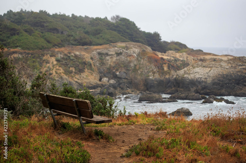 Wooden bench overlooking rocky cliffs on typical foggy day on Northern California coast
