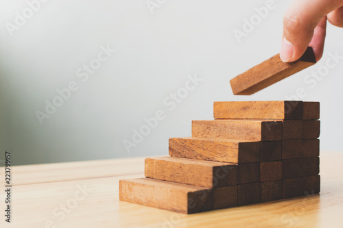 Hand arranging wood block stacking as step stair. Ladder career path concept for business growth success process
