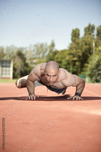 one young athletic man, exercising Push-up, shirtless strong muscular. outdoors running tracks (sports venue).