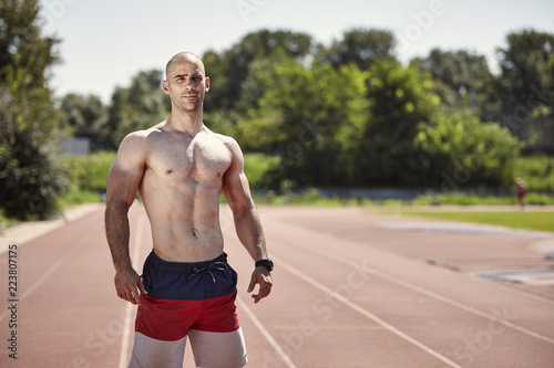 one athlete shirtless muscular standing posing, sport venue outdoors, running tracks.