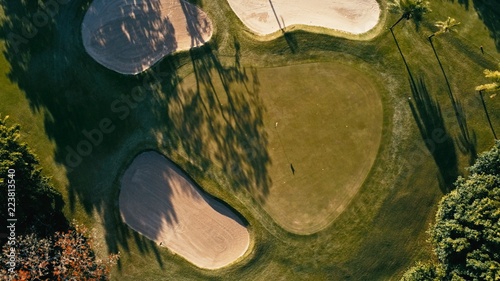 aerial image of a golf field course with a flag and hole and some sand and water pools with beautiful grass