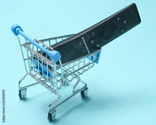 Tv remote in shopping cart for purchases on blue background, consumer concept, modern technology, minimalism. photo