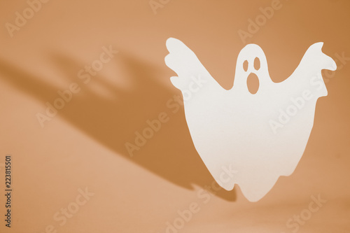 Halloween background concept. Funny ghost doing boo gesture and graphic shade behind on orange table.