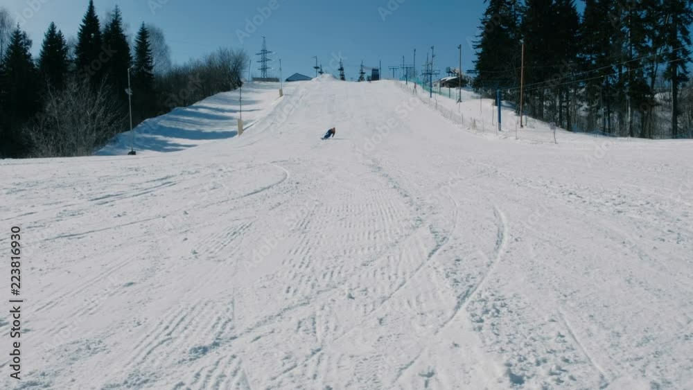 Teenage boy of 12 years in blue suit sliding on a snowboard from snow descent next sky lift. View from afar. Teenage boy of 12 years in blue suit sliding on a snowboard from snow descent next sky lift. View from afar.