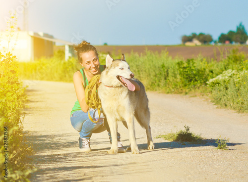 Happy young woman smiles and strokes a hussy dog among the fields. Paddling of pets.