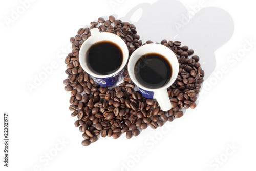 Two cups of black coffee and a heart made of coffee beans on white backgroung isolated