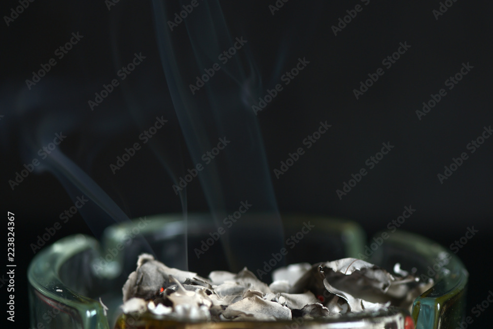A piece of paper burning in a glass ashtray close up