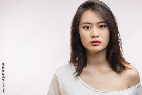 Confident sensual young Korean woman with long hair, dressed in white t-shirt looking at camera over white background. Youth and Beauty concept