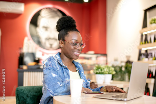 African American female blogger writing her new post in cosial media on digital tablet at modern urban cafe. photo