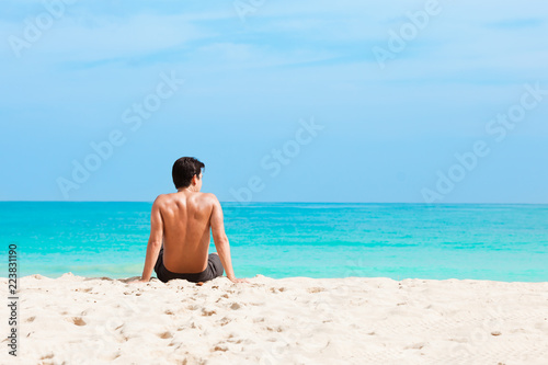 Young man sitting on a beautiful white sand beach. 