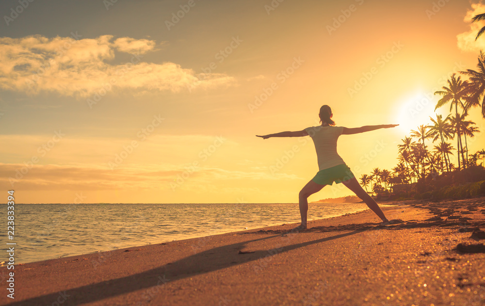 Young female doing stretching exercise on the beach at sunset. 