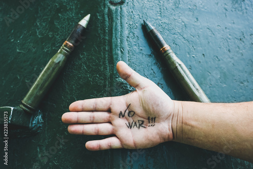 No war sign concept is written on the hand palm. Man is standing near the old tank from the Second World. Armored fighting vehicle as a memory monument in peaceful times.