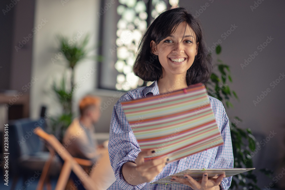 Beautiful Afro American business woman in smart casual wear is looking at camera and smiling while standing with a folder in office