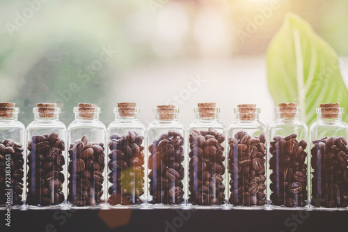 Coffee beans in glass bottles lined up in rows with leaves are the background, Warm light.