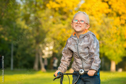 Счастливый улыбающийся мальчик в очках, на велосипеде осенью в парке 