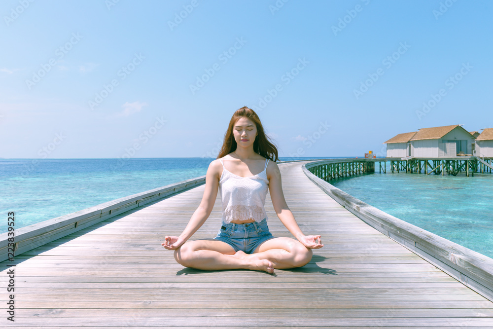 Beautiful Attractive Asian woman practicing yoga Lotus pose on wooden bridge on the beach in Maldives,Feeling so comfortable and relax in holiday,Healthy Concept