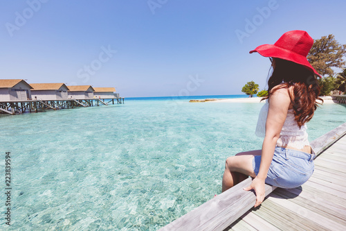 Portrait of Asian young woman sitting on wooden bridge looking in villas over water with beautiful turquoise sea in Maldives tropical island,feeling relax and comfortable,Travel and Vacation Concept
