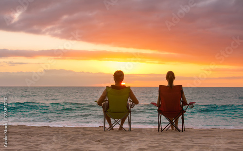 Young couple sitting on the beach relaxing watching the colorful sunset. 
