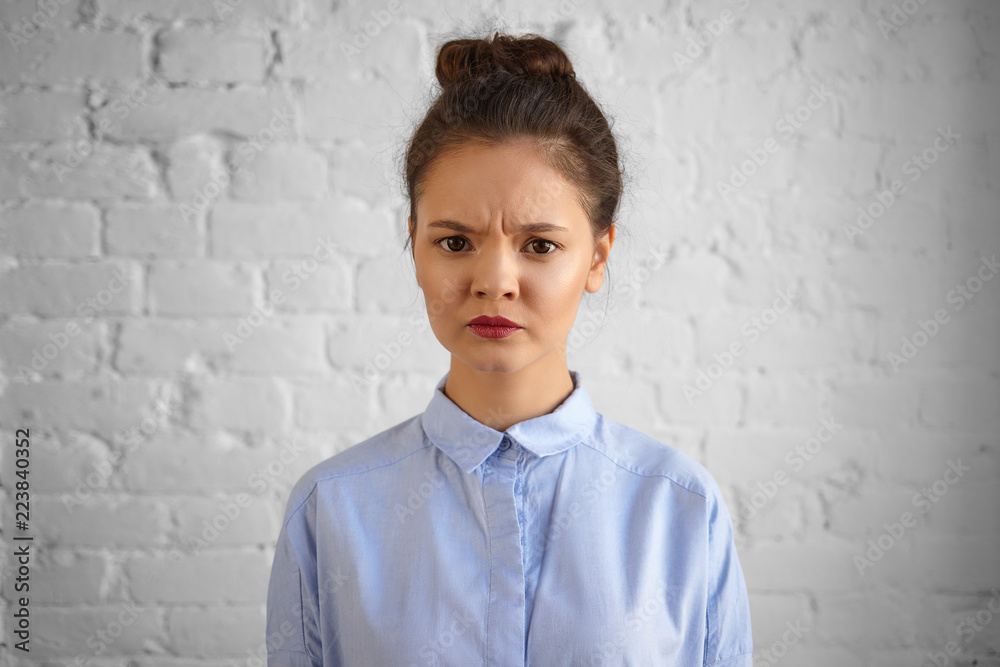 Horizontal shot of dark haired young female manager in formal wear frowning and making displeased grimace, being dissatisfied with work of her team. Negative human facial expressions and reaction Horizontal shot of dark haired young female manager in formal wear frowning and making displeased grimace, being dissatisfied with work of her team. Negative human facial expressions and reaction