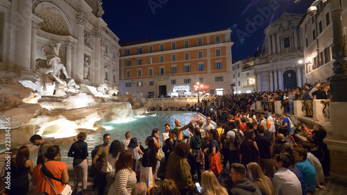 Masses of people taking photos of the beautiful Fontana di Trevi at night.