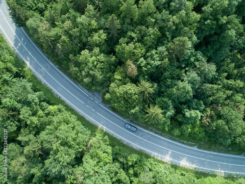AERIAL: Dark car drives through a curve of a road running through a forest.