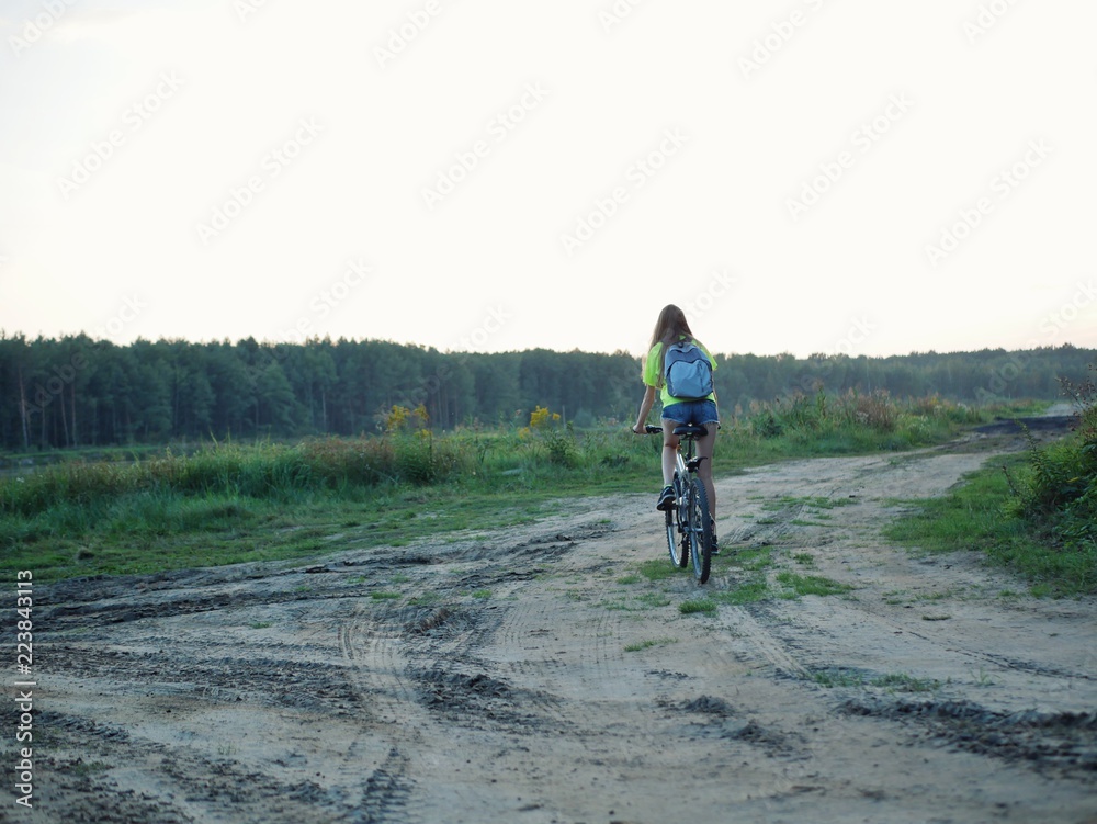 Polonne / Ukraine - 14 September 2018: girl in a green T-shirt with a backpack riding a bike Polonne / Ukraine - 14 September 2018: girl in a green T-shirt with a backpack riding a bike