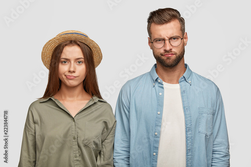 Indoor shot of sullen displeased family couple purse lips with unpleasant look, have to pay much money during vacation, express negative emotions, isolated over white background. Relationships concept