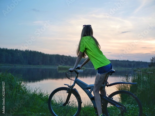 Fototapeta Naklejka Na Ścianę i Meble -  Polonne / Ukraine - 14 September 2018: The girl on a bike looks at the sunset on the lake